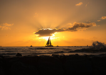 The setting sun in Waikiki was temporarily blocked by a lone cloud just as this sailboat was...