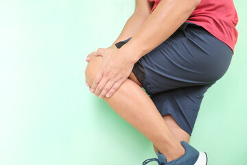 Knee pain and injury, joint arthritis concept. Young asian athlete man in running clothes grabbing his knees with copy space.