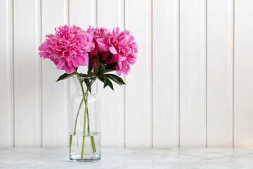 Pink peonies in a glass vase on a light background on the table. Empty space.