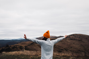Happy woman from behind running and raises her hands up in front of mountains