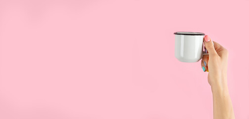 Arms raised up holding coffee cup on pink background.