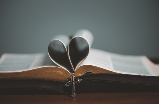 Open spiritual holy bible book with heart shape page folded in the middle and cross necklace.