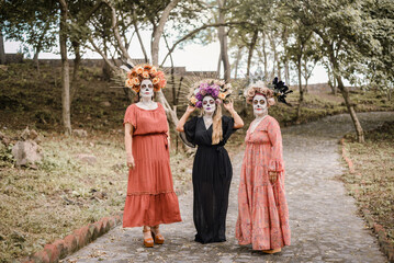 Fototapeta premium Group portrait of three women with the makeup of the catrinas.. Makeup for the celebration of Day of the Dead in Mexico. Outdoors portrait.
