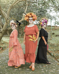 Group portrait of three women with the makeup of the catrinas.. Makeup for the celebration of Day of the Dead in Mexico. Outdoors portrait.