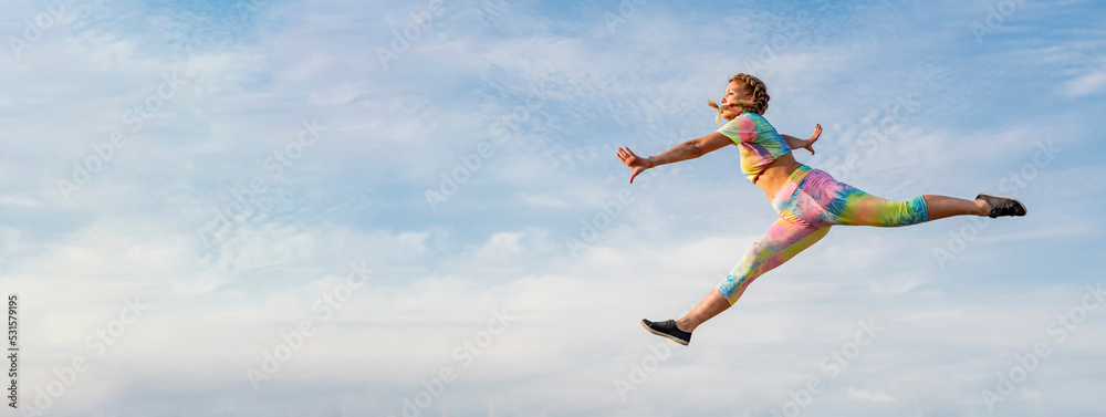 Wall mural young girl gymnast in bright tracksuit flies in long jump against background of blue summer evening 