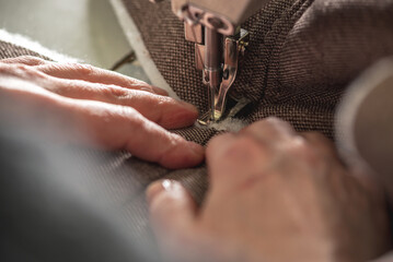 Women's hands in the process of sewing on professional equipment. Sewing fabric in production. Close-up