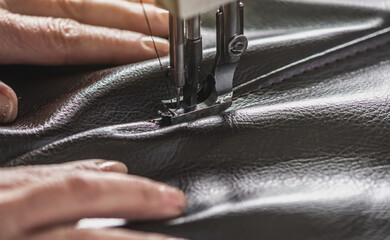 Women's hands in the process of sewing on professional equipment. Sewing leather in production....