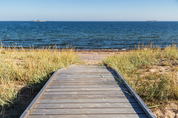 Wooden boardwalk leading to an empty beach in Hanko, Finland, on a sunny day in the summer. Focus on the front, shallow depth of field.