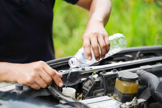 Closeup and crop image of hand of human checking car engine and filling water to the car radiator on blurred background.