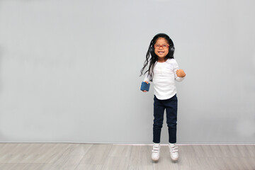 4-year-old brunette Latin girl with glasses listens to music in her headphones connected to her cell phone dances, sings and enjoys the rhythm happy and excited
