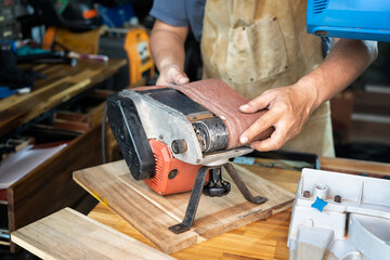 carpenter wearing apron and Install or remove abrasive belt of Belt Sander on wooden tabel in the...