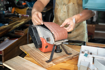 carpenter wearing apron and Install or remove abrasive belt of Belt Sander on wooden tabel in the...
