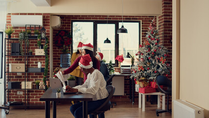 Diverse people working in festive office, planning report and wearing santa hats. Doing startup work on fast forward speed during winter holiday season with christmas tree. Timelapse.