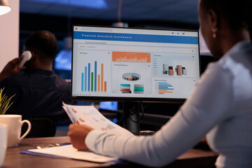 Office employee analyzing business charts on computer and documents, looking at online research...