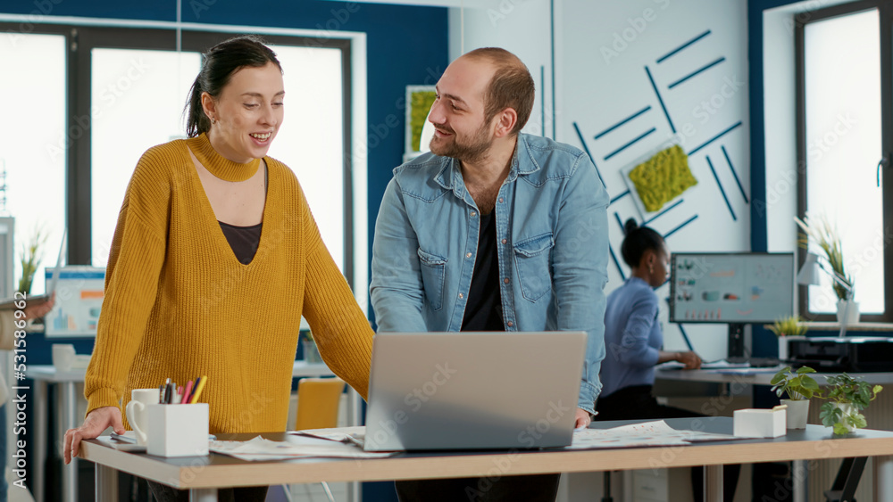 Poster smiling coworkers in office looking at laptop screen comparing business analytics with sales charts 