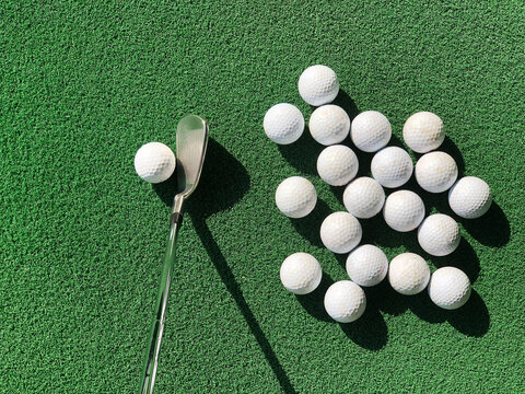 Groups of practice golf ball on an artificial grass mat with one club iron address at one ball under the morning sunlight.