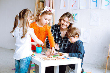 Children with interest play with educational toys on desk sitting on floor. Smiling educator point...