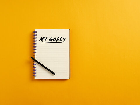 Notepad and black pen on yellow background with the handwritten word my goals. Planning personal goals