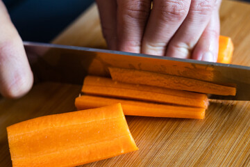 man hands cutting carrots close up on wooden board