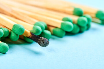 Close-up of a group of matches with green heads and with one burnt match on a blue background