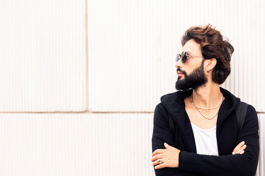 beautiful young man with sunglasses leaning in a white wall looking to the side, concept of urban lifestyle and stylish clothing, copy space for text