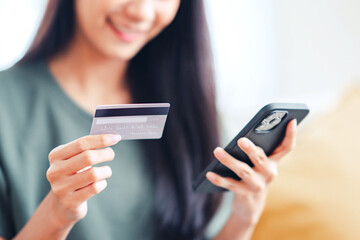 Closeup - Happy young woman holding credit card using instant mobile payments at home. Smiling Female customer shopper making purchase on smartphone receiving cash back concept. E-banking app service.