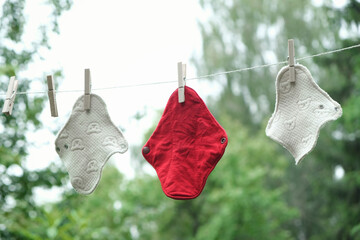 Three reusable cloth sanitary menstrual pads hanging to dry on clothesline in the garden. Zero...