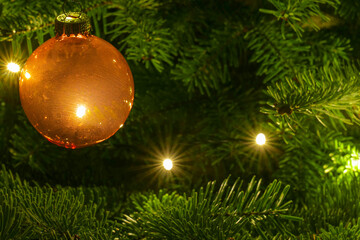 Close-up of a golden-brown Christmas tree ball on the tree with string of lights