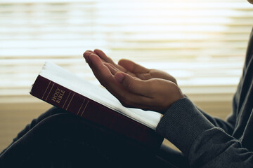 Hands open palm up in prayer on a Holy Bible in church concept for faith, spirituality, and religion, a woman praying on holy bible in the morning. woman hand with Bible praying. prayer bible