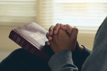 Hands clasped in prayer on the bible praying to God in the morning, spirituality and religion,...