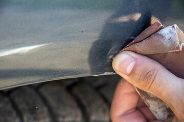 Removing rust from car parts. Car body corrosion. sandpaper in the hands of a man.