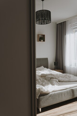 Fototapeta na wymiar Aesthetic bedroom interior design. Neutral Scandinavian comfortable living room with bed, crumpled bed linens, window with curtains. Sunlight shadows
