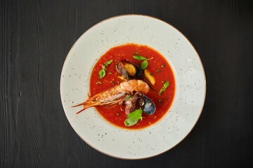 Tomato soup with seafood, shrimp, octopus, mussels and other shellfish for cooking dinner on a black background. Healthy food handmade