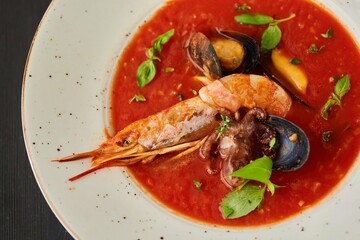 Tomato soup with seafood, shrimp, octopus, mussels and other shellfish for cooking dinner on a black background. Healthy food handmade
