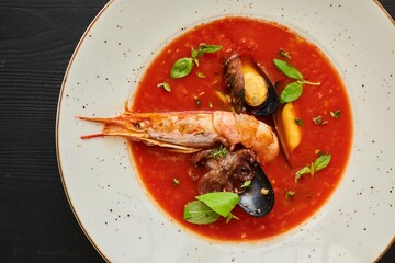 Tomato soup with seafood, shrimp, octopus, mussels and other shellfish for cooking dinner on a black background. Healthy food handmade