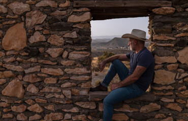 Obraz na płótnie Canvas Side view of adult man in cowboy hat sitting on window frame