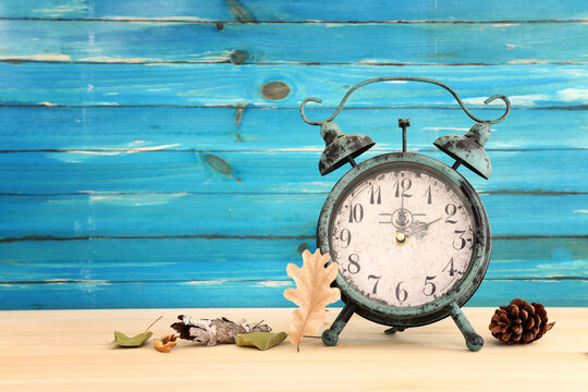 Image of autumn Time Change. Fall back concept. Dry leaves and vintage alarm Clock on rustic wooden table