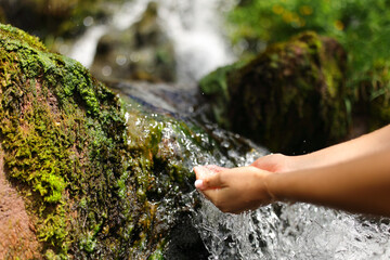 Woman hands in a waterfall catching raw water