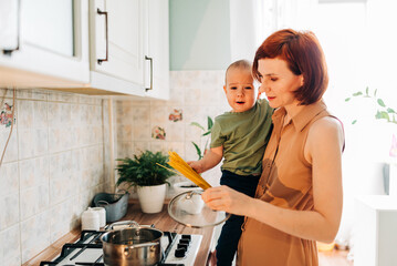 Happy mom with her child cooking at the kitchen. Cozy home and routine duties