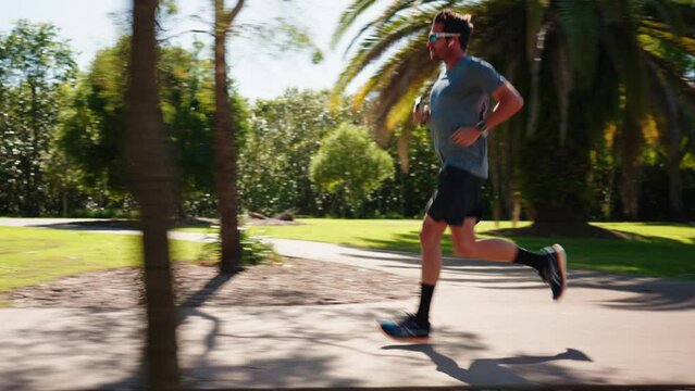 Side Profile Of Man In Sunglasses Jogging On Park Footpath On Sunny Day, 4K Slow Motion