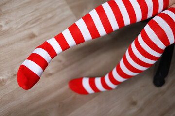 Obraz premium Female legs in Christmas knee socks. Woman sitting in office chair, concept of New Year celebration, girl in Santa costume