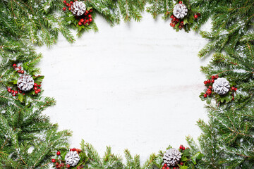 Fototapeta na wymiar Frame of fir tree branches with snow decorated with red natural hawthorn berries and cones colored in white color on bright painted background. New Year and Christmas concept. Top view, copy space
