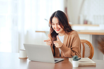 Fototapeta na wymiar Happy positive young asian woman enjoying online communication at home, Female using wifi while video conferencing with friend, sitting in front of open laptop, copy space.