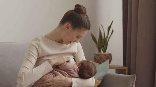 Medium slowmo of young happy mother breastfeeding her newborn baby at home