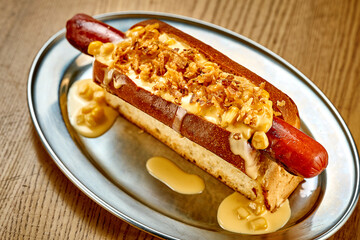Hot dog with cheese sauce, caramelized onions. Close-up, selective focus. Noise added in post-production