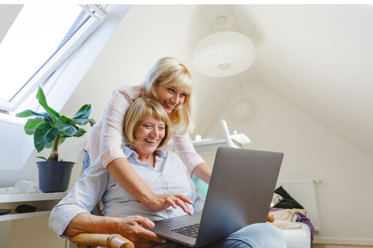Happy blond woman with mother using laptop at home
