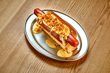 Hot dog with cheese sauce, caramelized onions. Close-up, selective focus. Noise added in post-production