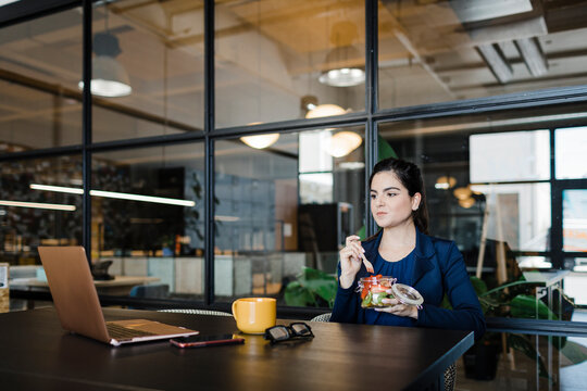 Young businesswoman having fruits and watching laptop in office