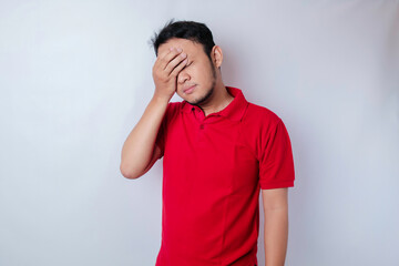 A portrait of an Asian man wearing a red t-shirt isolated by white background looks depressed
