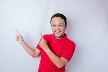 Excited Asian man wearing red t-shirt pointing at the copy space on top of him, isolated by white...